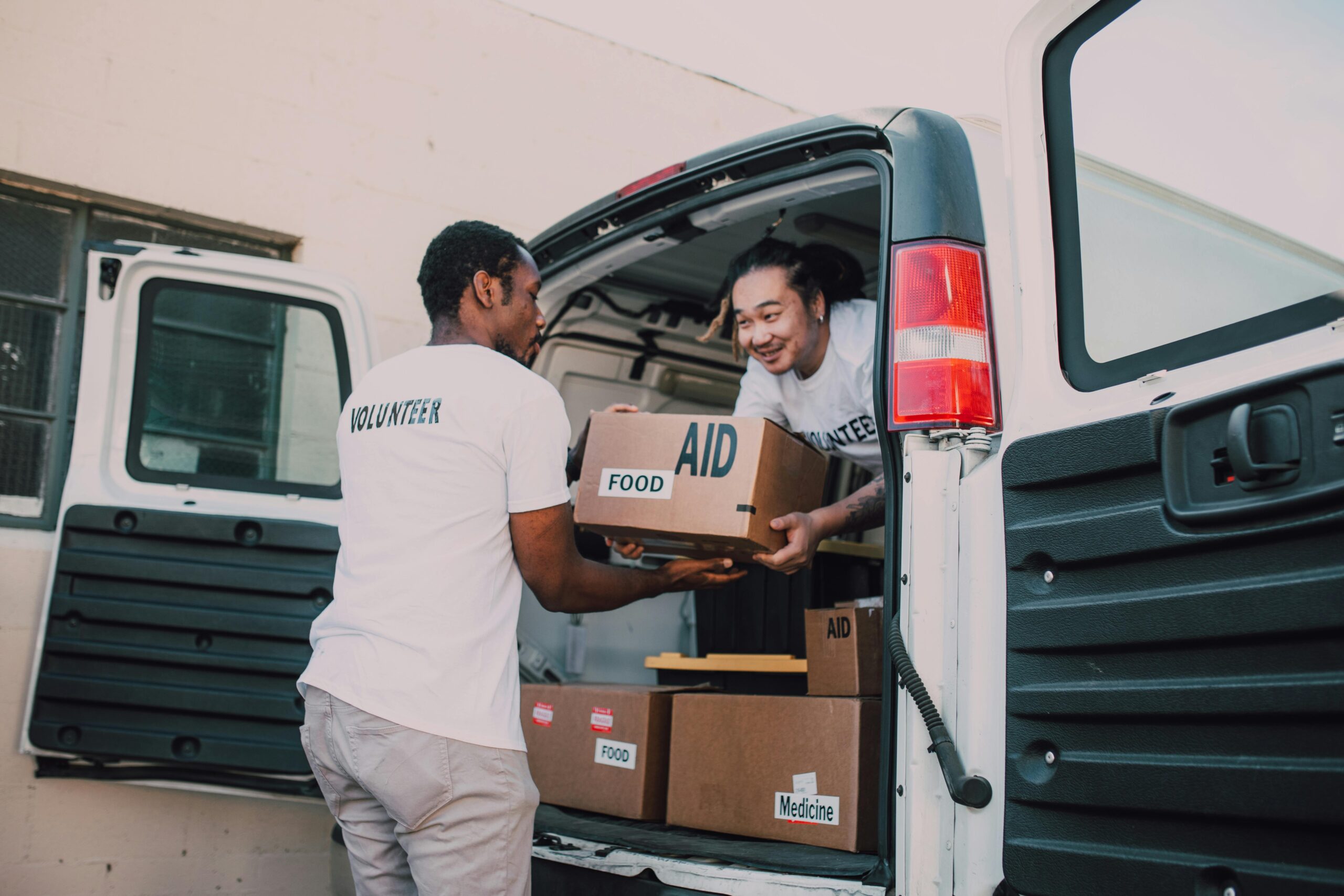 Man in White T-shirt and White Pants Standing Beside White Van